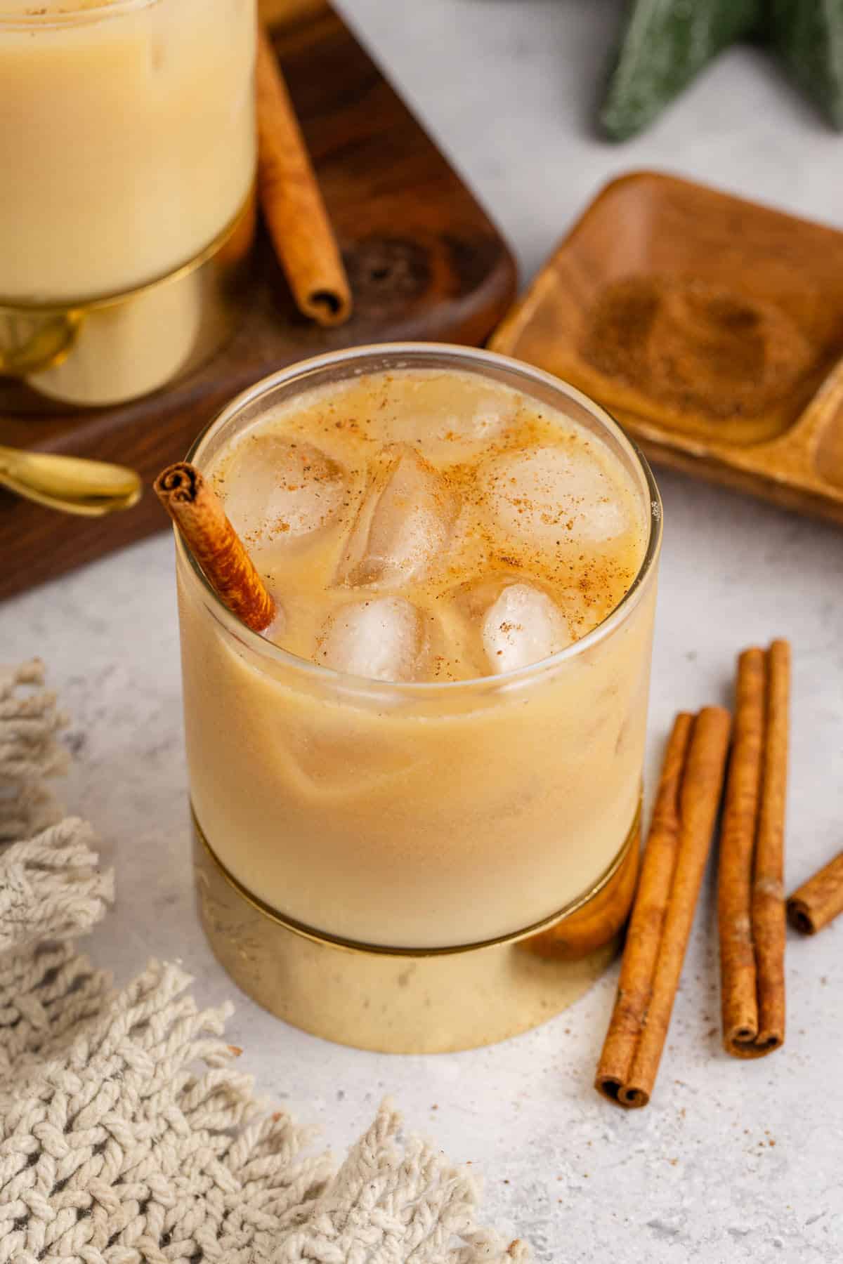 Spiked Eggnog with Rum in a Clear Glass Over Ice with Dusting of Ground Cinnamon and Cinnamon Stick Garnish