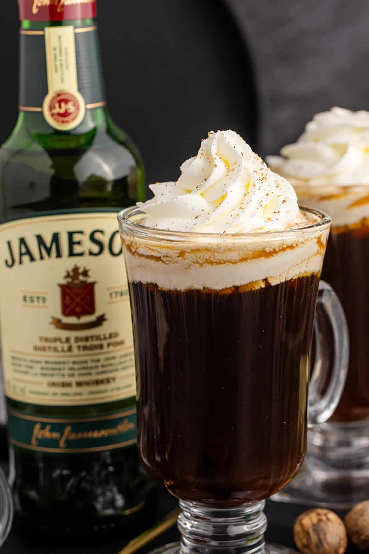 Espresso Irish Coffee in a Clear Mug Topped with Whipped Cream and Ground Nutmeg with Jameson Bottle in Background