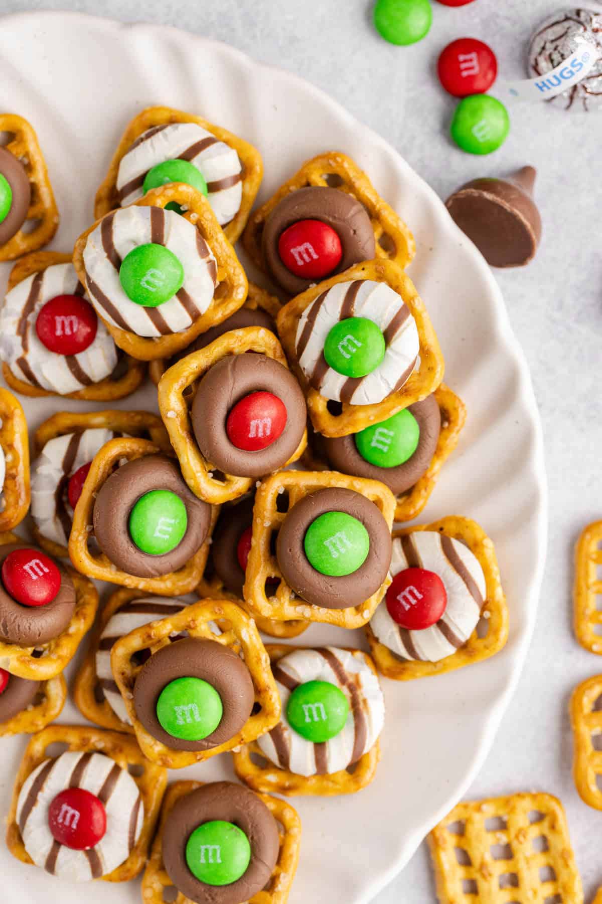 Christmas Pretzel Treats stacked on a plate close up with M&Ms, pretzel snaps and Hersheys chocolates in the back