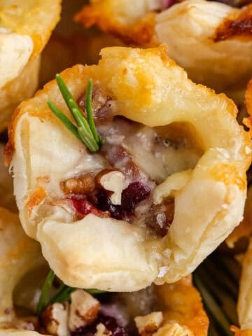 Close Up Cranberry Brie Bites Stacked on a Plate and Garnished with Rosemary Sprigs