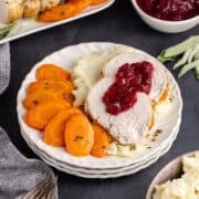 Boneless Turkey Breast Sliced and Served on a Plate with Cranberry Sauce Mashed Potatoes and Glazed Carrots with Fresh Sage
