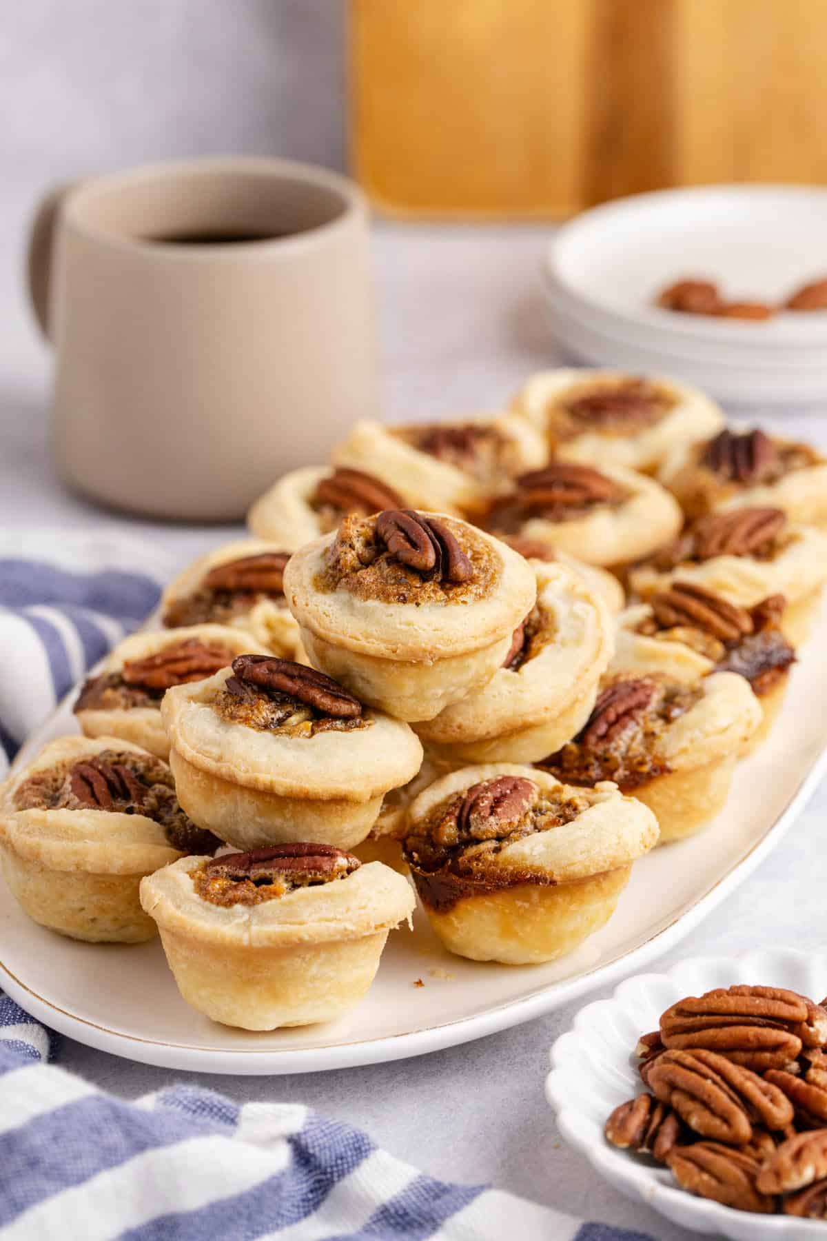 Mini Pecan Pies stacked on a platter with a coffee in the back