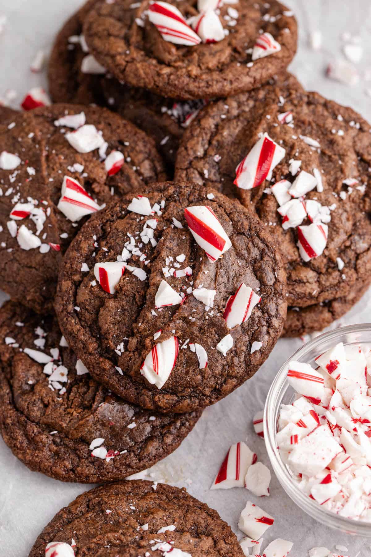 Peppermint Brownie Cookies stacked on parchment paper with crushed peppermint all around