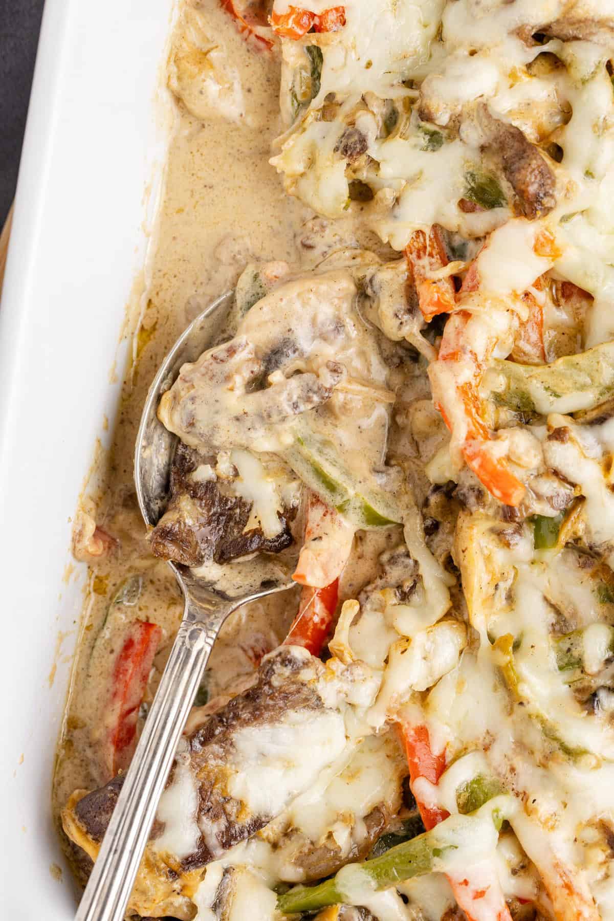 Philly Cheesesteak Casserole in the dish with a serving spoon and some missing close up