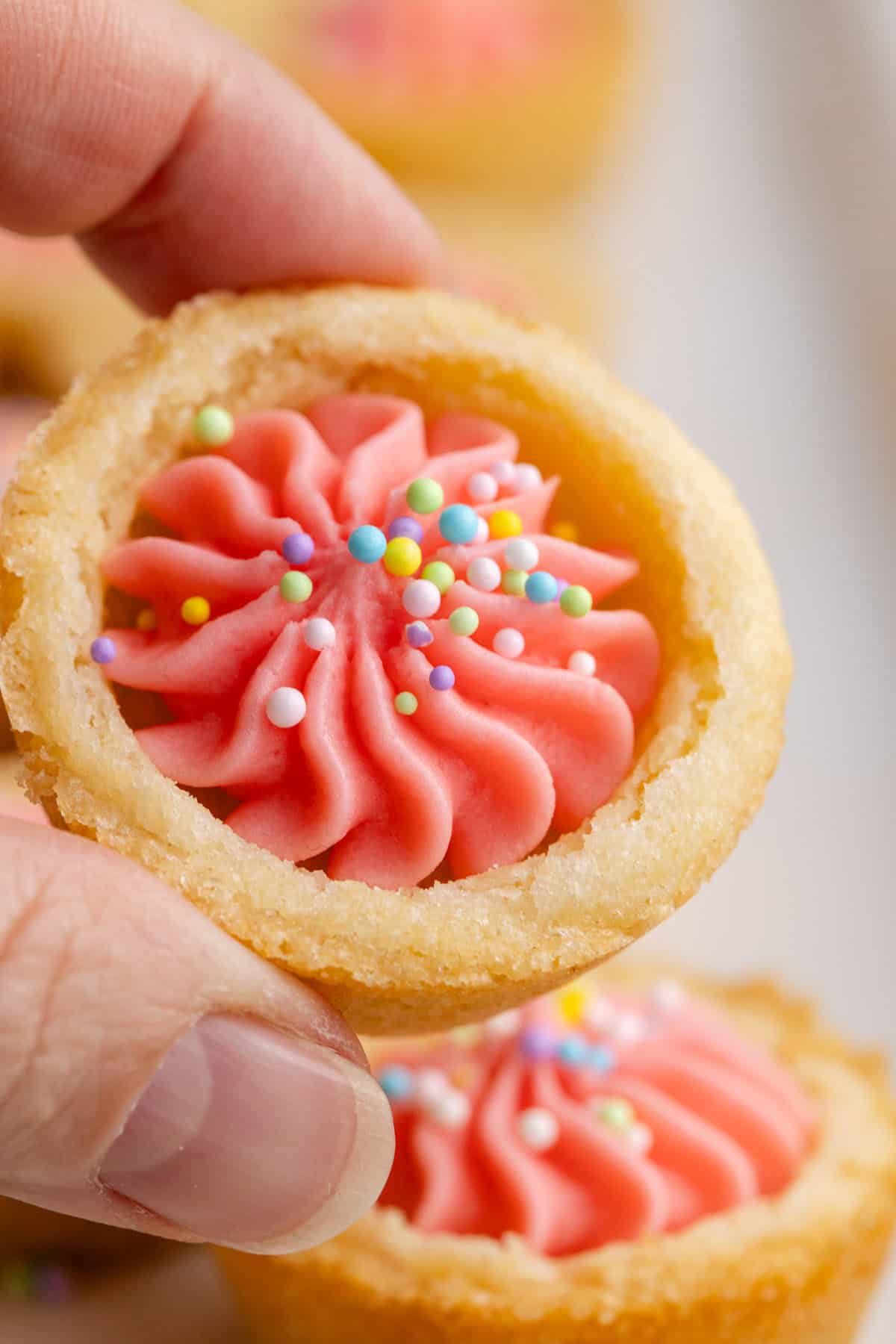 Easter Sugar Cookie Cups with pink icing and sprinkles being picked up
