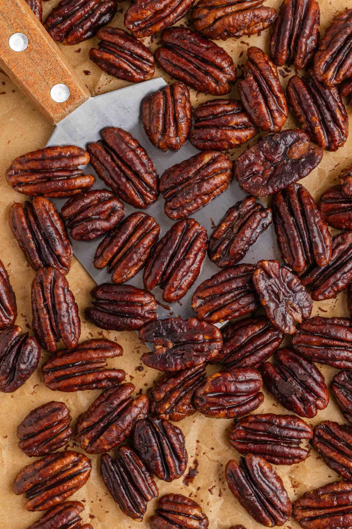 Overhead View of a Metal Spatula Lifting Keto Candied Pecans on a Parchment Paper Lined Baking Sheet