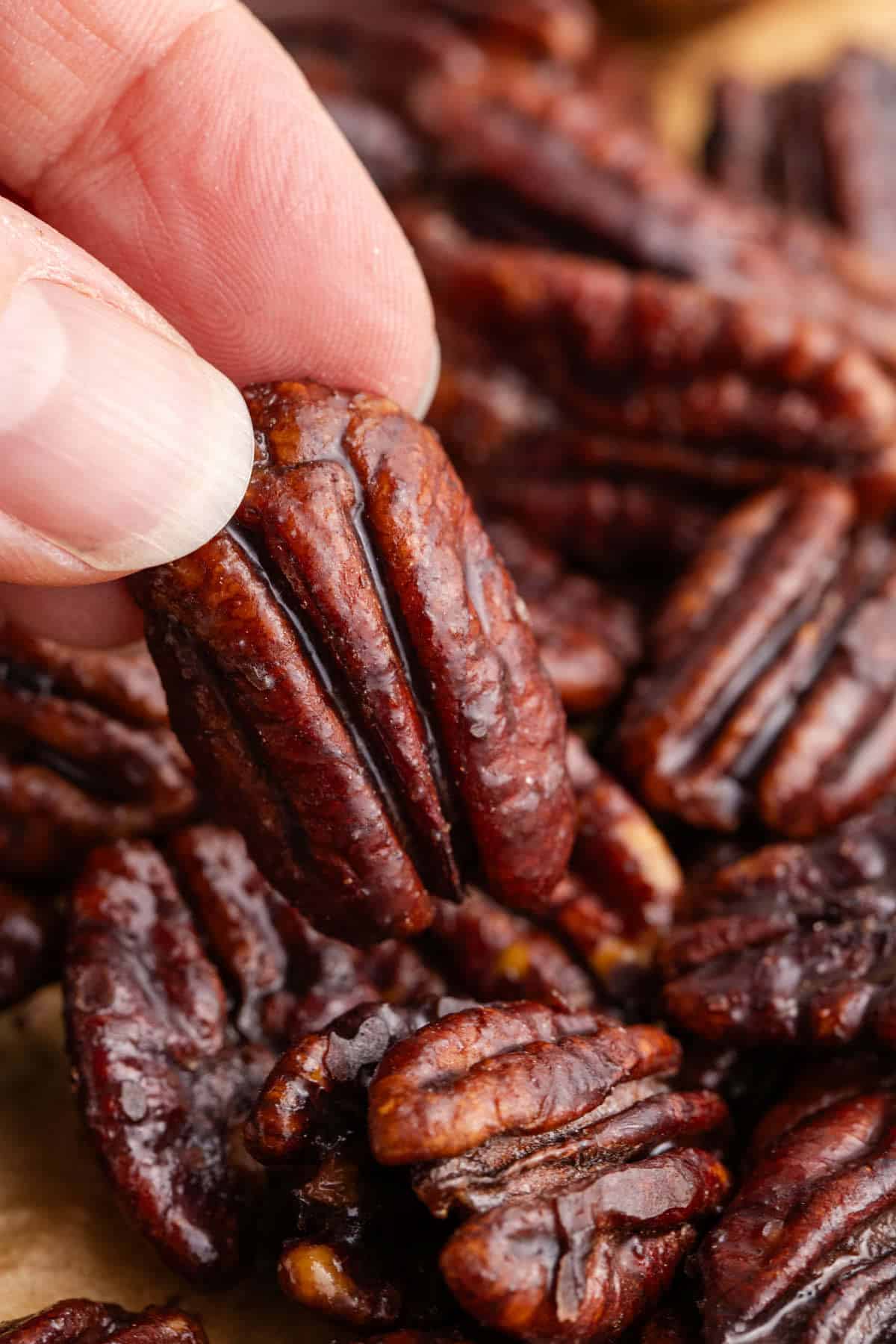 Hand Picking Up Keto Candied Pecans with Pecans on Parchment Paper in Background
