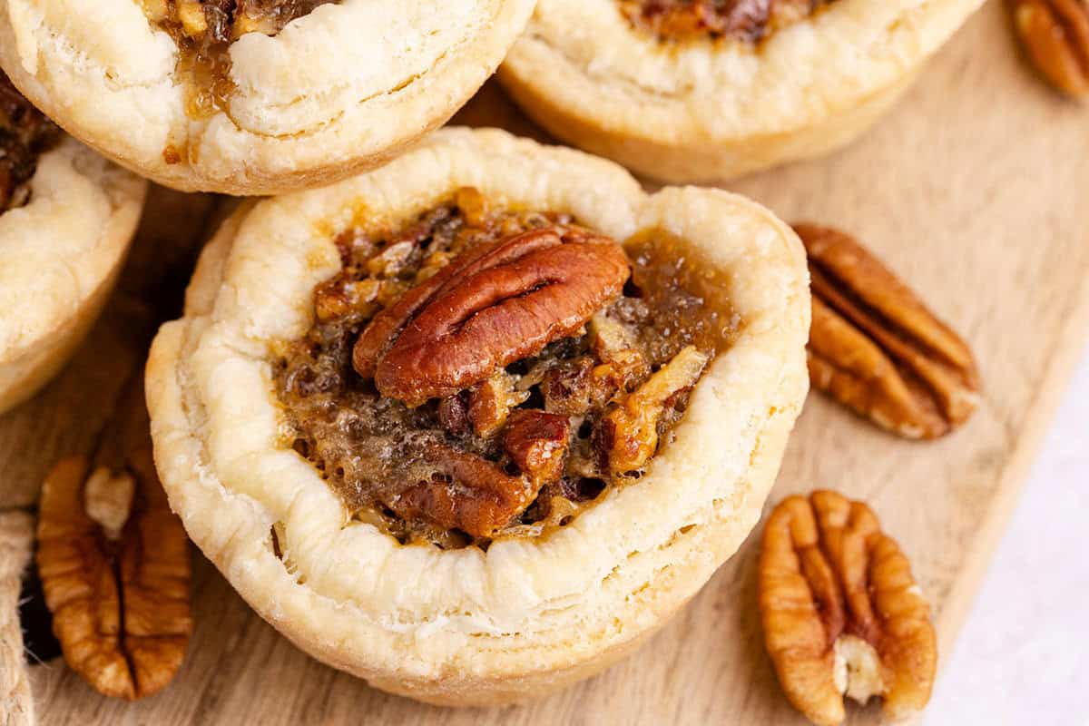 Pecan Tarts stacked on a cutting board board with pecans around it