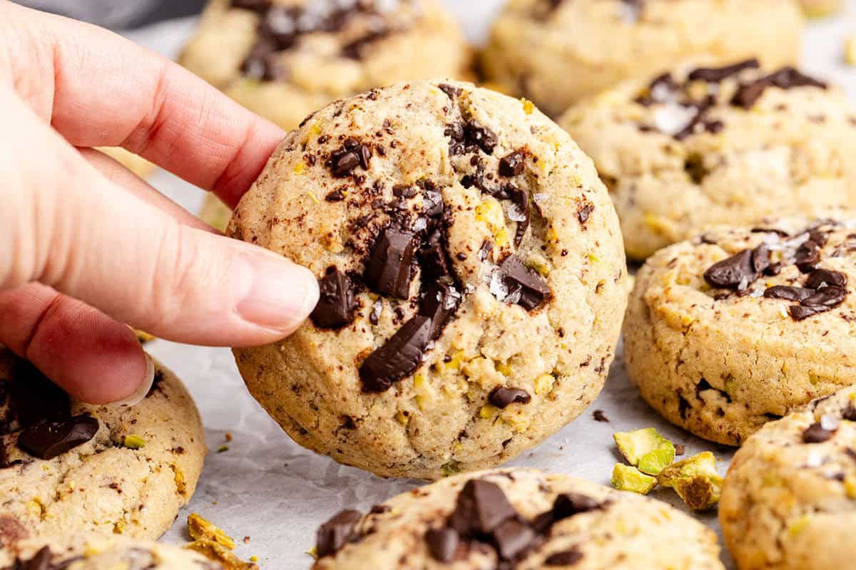 Pistachio Chocolate Chip Cookies on parchment paper being picked up