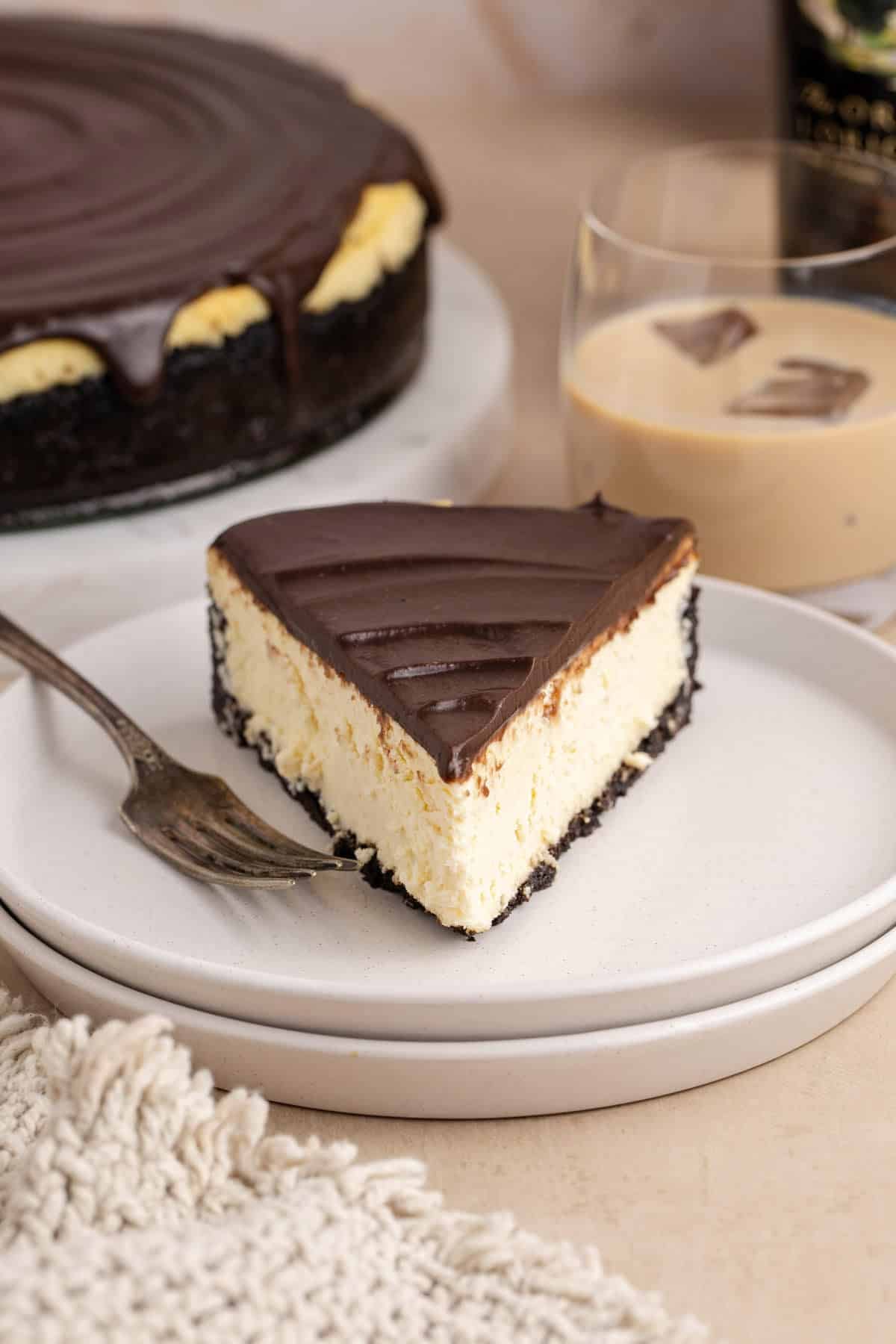 Baileys Cheesecake on a plate with a glass in the back