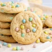Cadbury Mini Egg Cookies stacked on a baking sheet with mini eggs all around
