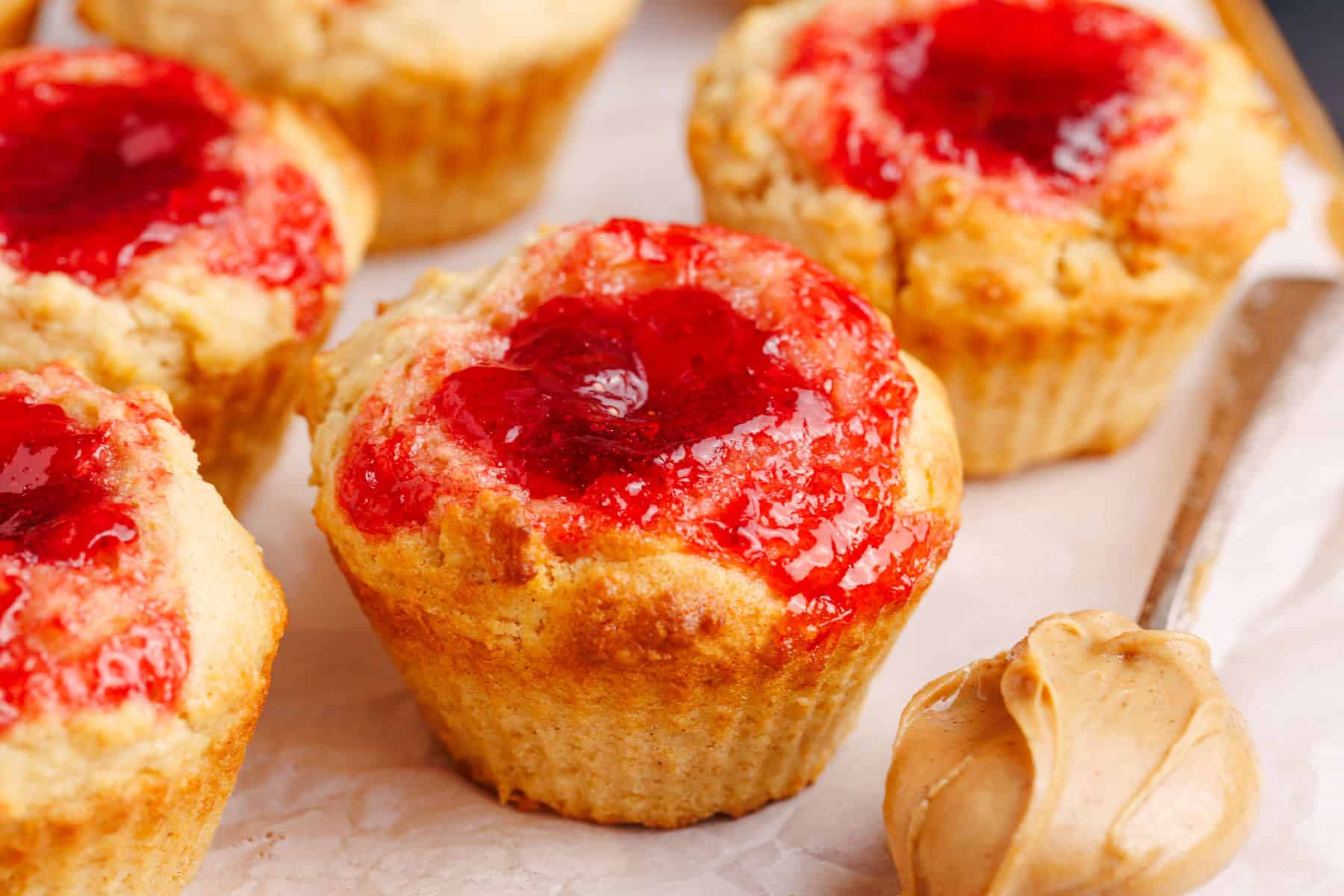 Peanut Butter and Jelly Muffins on parchment paper with a spoonful of peanut butter beside it