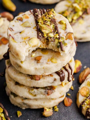 Pistachio Shortbread Cookies stacked on top of each other with cookies and nuts around