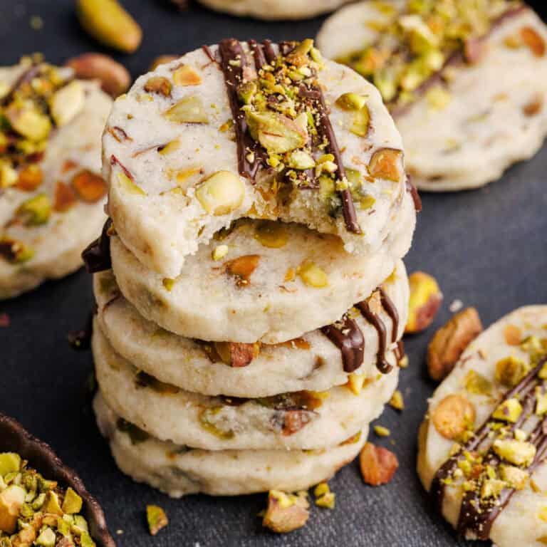 Pistachio Shortbread Cookies stacked on top of each other with cookies and nuts around