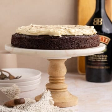 Baileys Irish Cream Cake on a cake stand with Baileys in the background