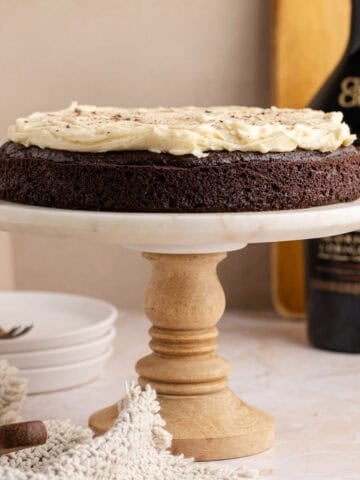 Baileys Irish Cream Cake on a cake stand with Baileys in the background