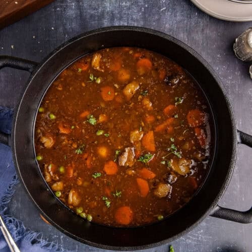 Guinness Lamb Stew from above in a Dutch oven cooked with bread and bowls beside