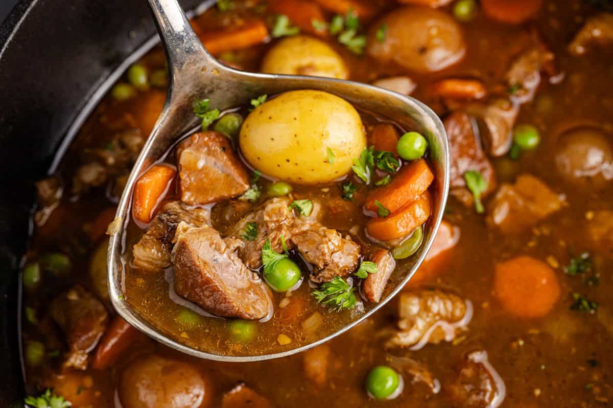 Guinness Lamb Stew in a ladle overtop of a Dutch oven