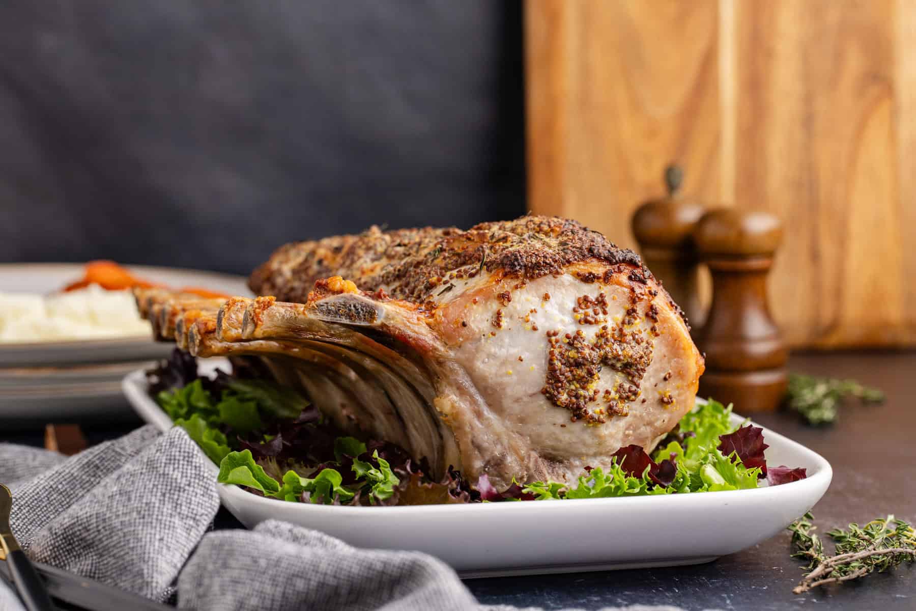 Pork Prime Rib cooked on a platter with plates in the back