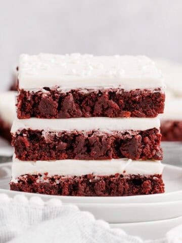 Red Velvet Cookies Bars stacked on a plate with icing and sprinkles