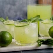 Cucumber Agua Fresca on a cutting board with limes and mint and a pitcher in the back