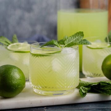 Cucumber Agua Fresca on a cutting board with limes and mint and a pitcher in the back