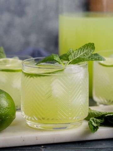 Cucumber Agua Fresca on a cutting board with limes and mint and a pitcher in the back