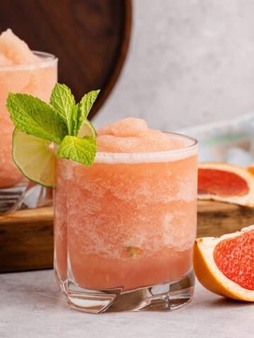 Non alcoholic frozen paloma served in a glass and garnished with a lime round and fresh mint with slices of grapefruit beside