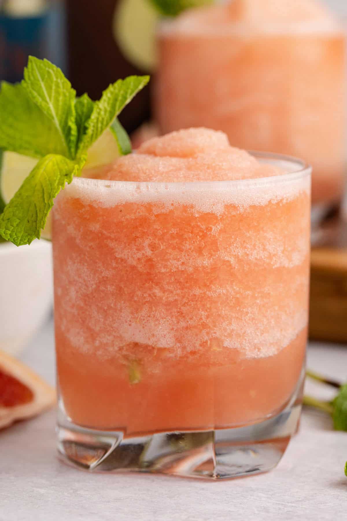 close up of Non alcoholic frozen paloma served in a glass and garnished with a lime round and fresh mint