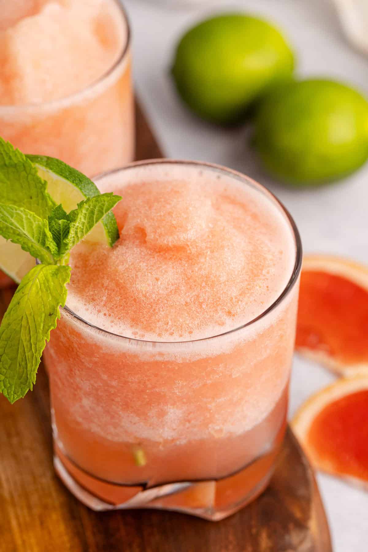 top down view of non alcoholic frozen paloma served in a glass and garnished with a lime round and fresh mint with slices of grapefruit beside