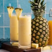 Two glasses of non-alcoholic frozen Pina coladas with a pineapple in the back