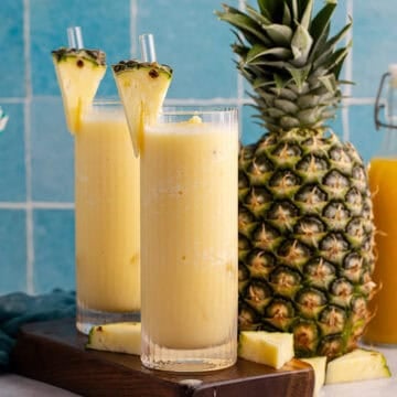 Two glasses of non-alcoholic frozen Pina coladas with a pineapple in the back