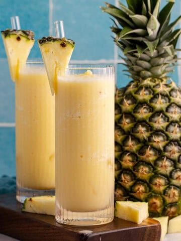 Two glasses of non-alcoholic frozen Pina coladas with a pineapple in the back