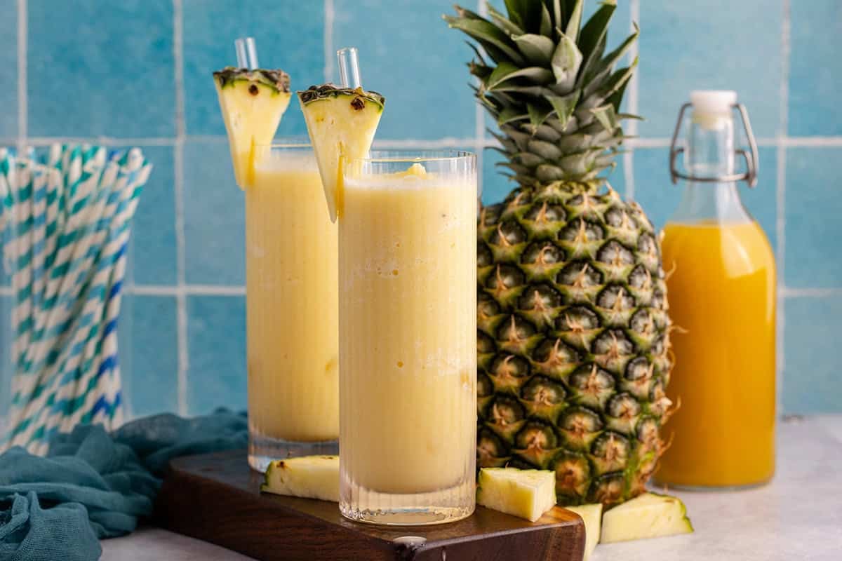 Two glasses of non-alcoholic frozen Pina coladas with a pineapple in the back