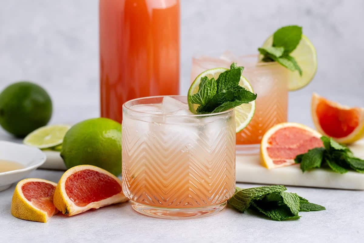 Non Alcoholic Paloma on a with mint and limes for garnish on a counter