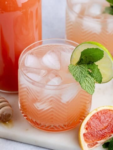 Non Alcoholic Paloma on a cutting board with mint and limes around