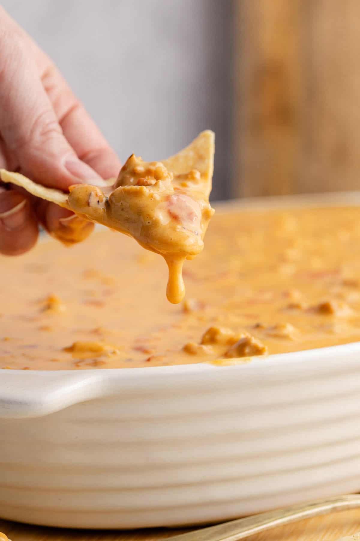 Spicy Sausage Queso in an oval dish with a corn chip scooping some dip