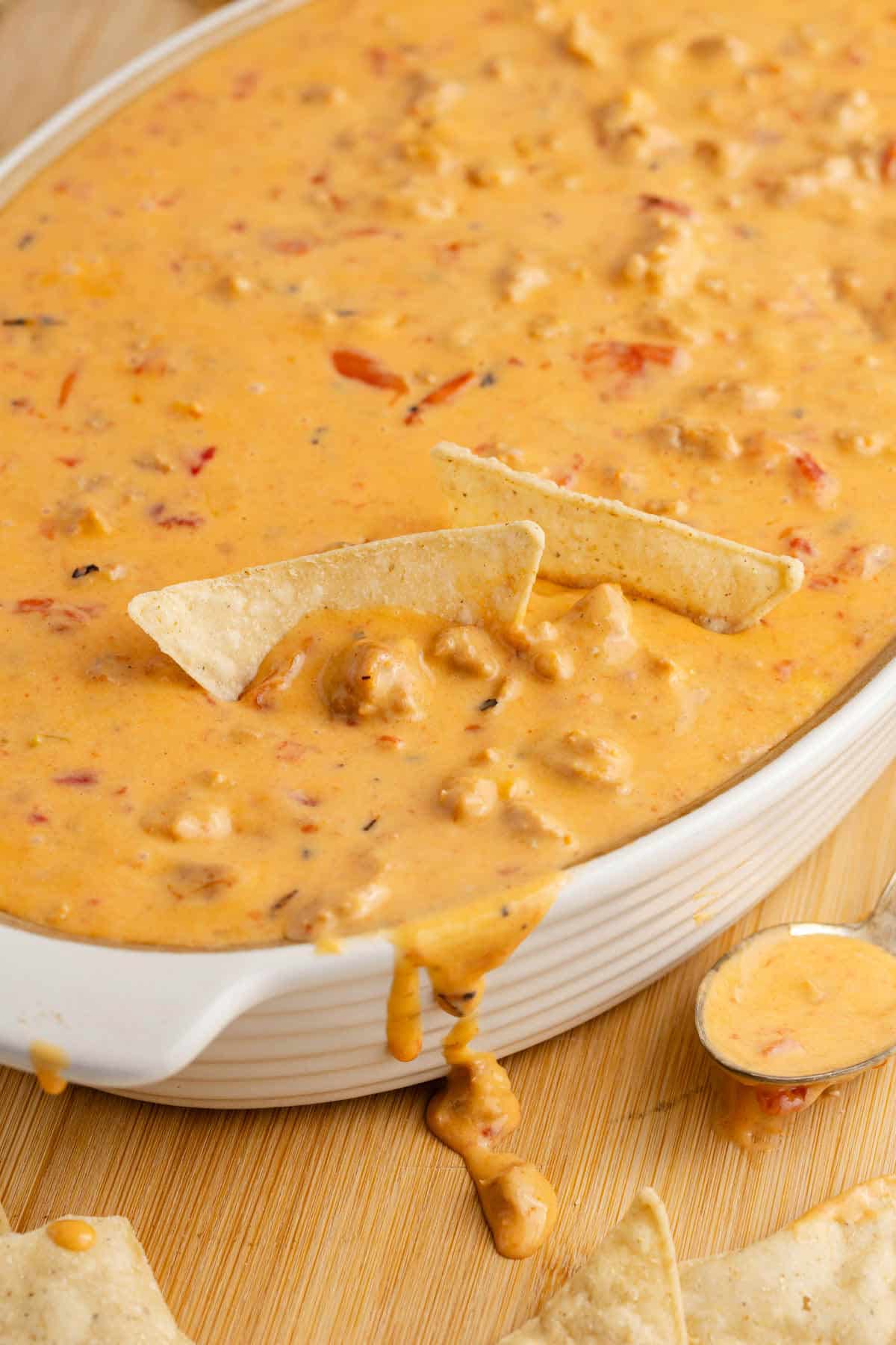 Spicy Sausage Queso in an oval dish with cheese dripping down the front and corn chips inside