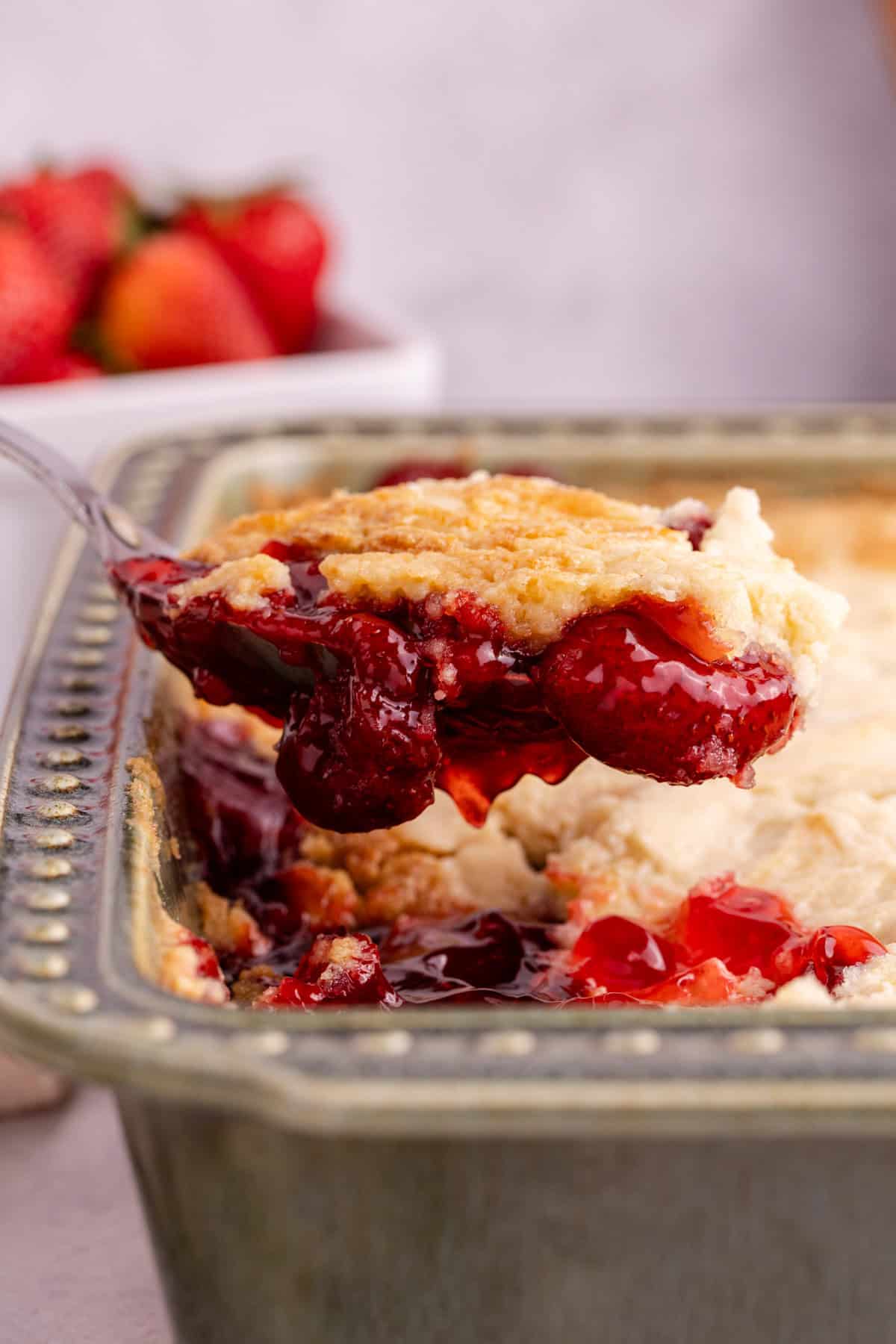 Strawberry Dump Cake with a serving spoon scooping and hovering above the pan