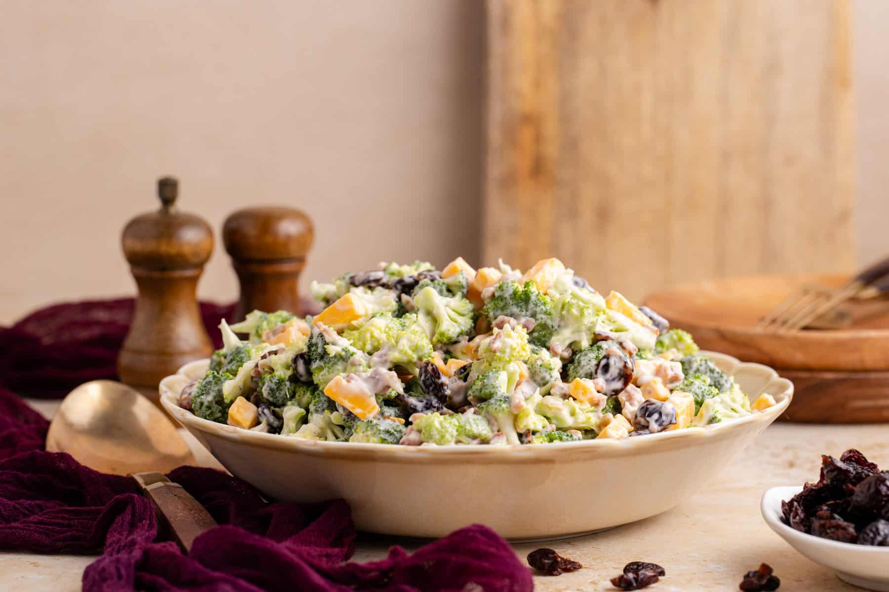 Broccoli Salad with Cranberries in a serving bowl with plates in the back