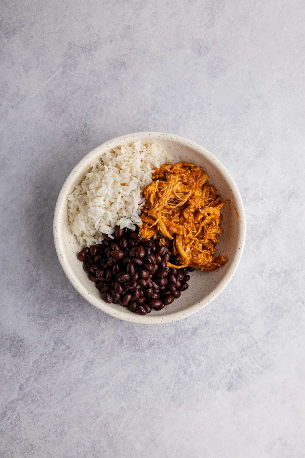 Chicken Tinga bowl being made on a counter with rice and beans