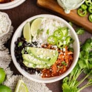 Chicken Tinga bowl from above garnished with cilantro, avocado and jalapeños and a dressing in the background