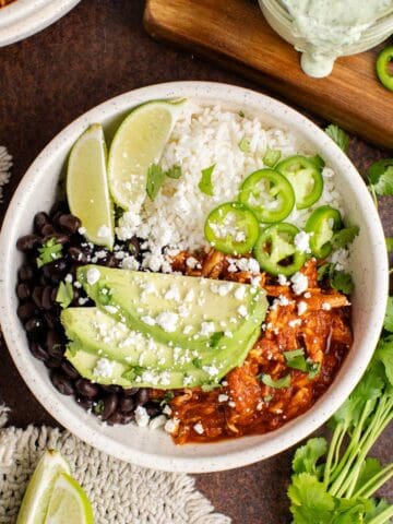 Chicken Tinga bowl from above garnished with cilantro, avocado and jalapeños and a dressing in the background
