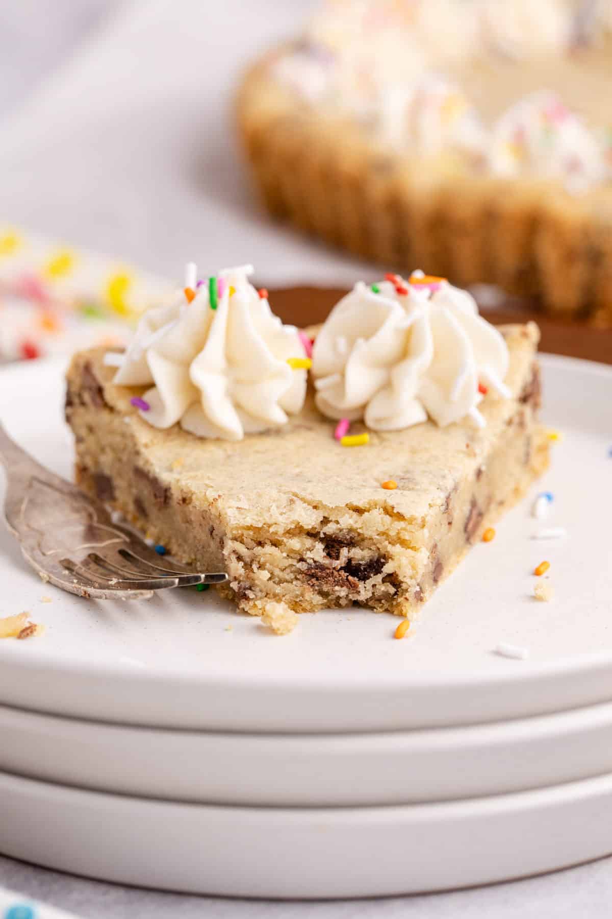 Chocolate chip cookie cake close up on a stack of plates with a piece taken