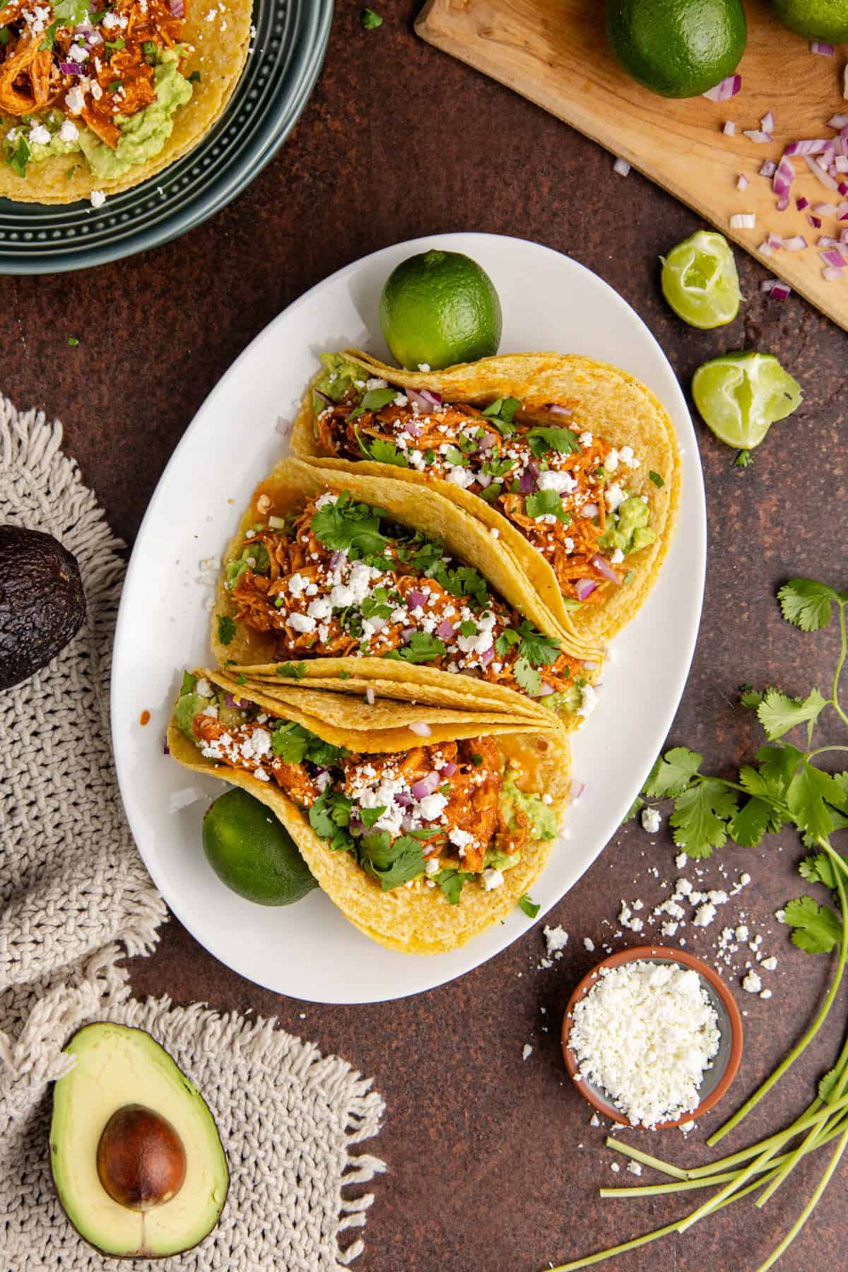 Instant Pot Chicken Tinga Tacos from above on a platter with another taco on a stack of plates