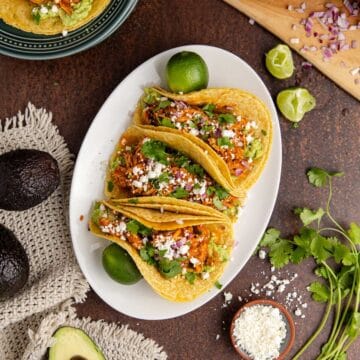Instant Pot Chicken Tinga Tacos from above on a platter with another taco on a stack of plates