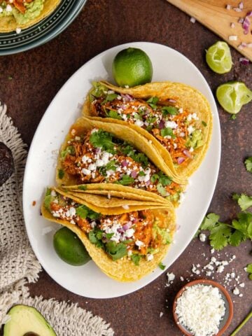 Instant Pot Chicken Tinga Tacos from above on a platter with another taco on a stack of plates
