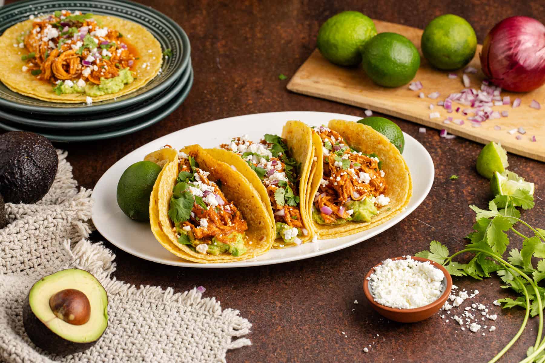 Instant Pot Chicken Tinga Tacos on a platter with plates, limes and onions in the background