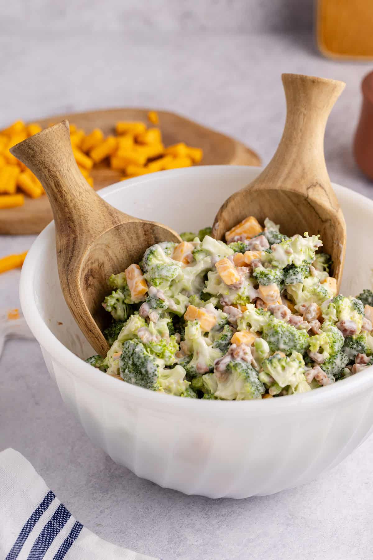Keto broccoli salad in a bowl with serving spoons on a counter with cheese in the background