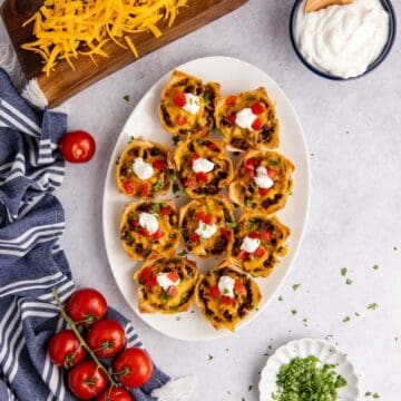 Mini Taco Cups on a platter with sour cream, tomatoes and cilantro from above